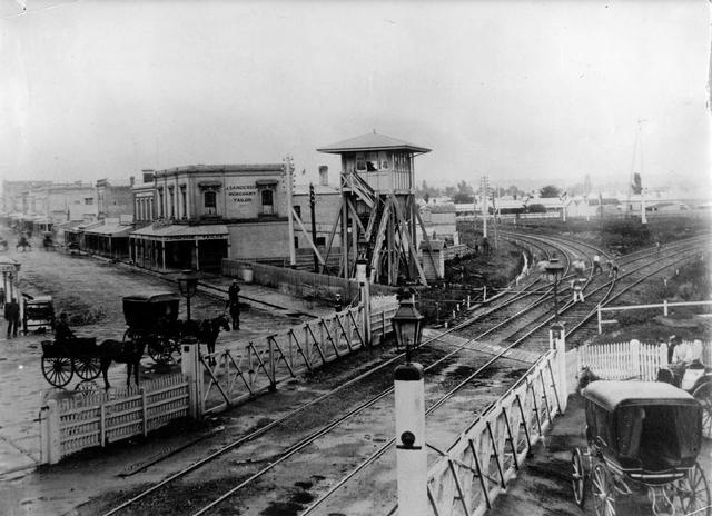 The photograph shows Swan St and the Swan St shops from a western angle. According to the information accompanying the image: 'About 1884. The Swan St. railway crossing. J. Sanderson's building is still standing. The line on the right went to the Cremorne